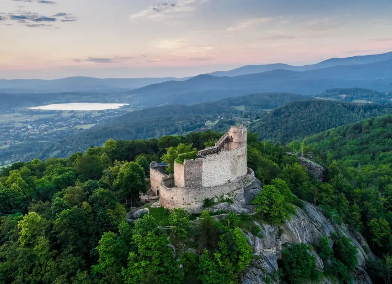 Zamek Chojnik g&oacute;ruje nad zielonymi wzg&oacute;rzami i jeziorem. Ruiny zamku na skale otoczone lasem.