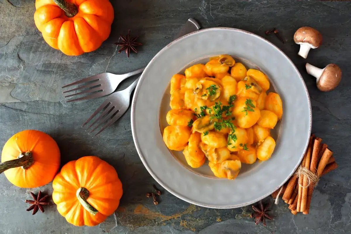Pyszne gnocchi z dyni w kremowym sosie, udekorowane natką pietruszki. Obok dynie, grzyby i laski cynamonu.