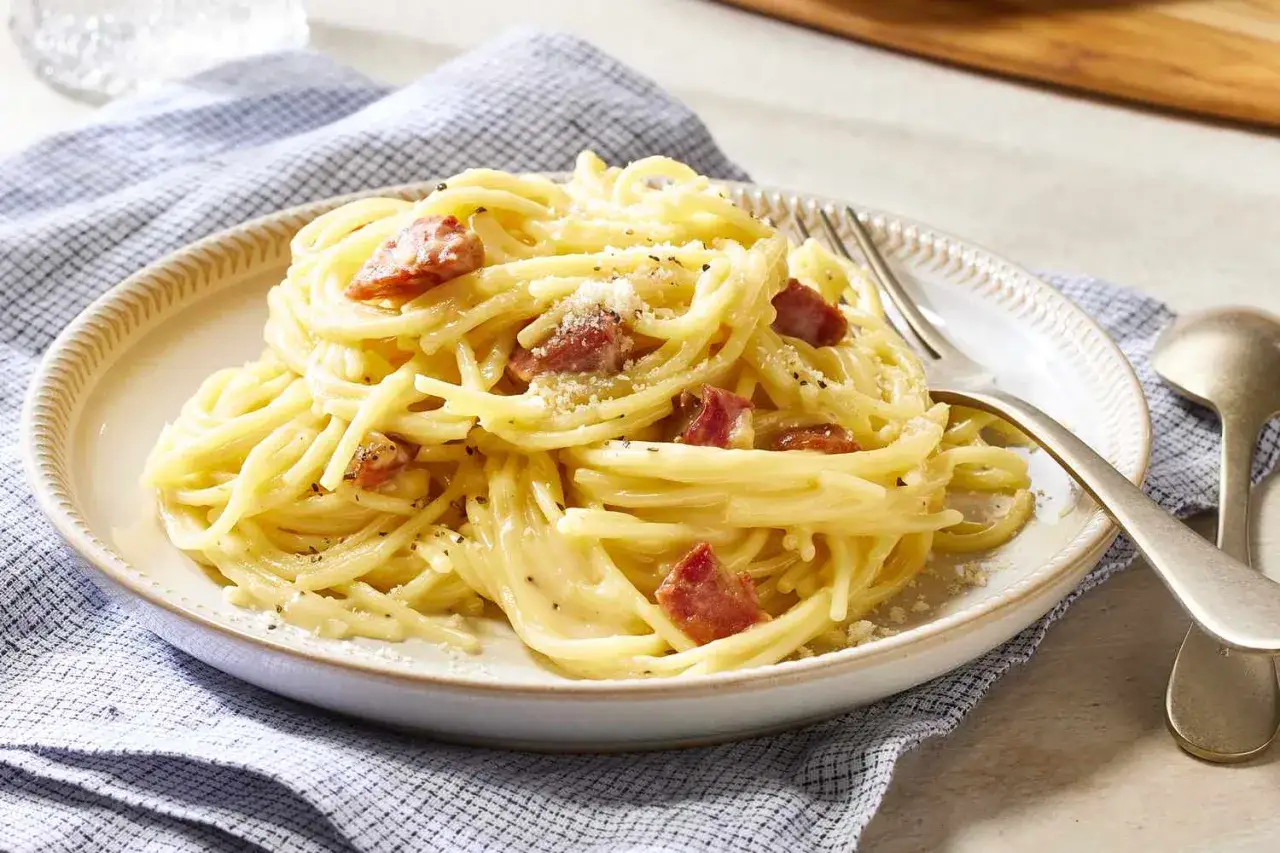 Pyszne spaghetti carbonara ze śmietaną, okraszone kawałkami boczku i posypane parmezanem.