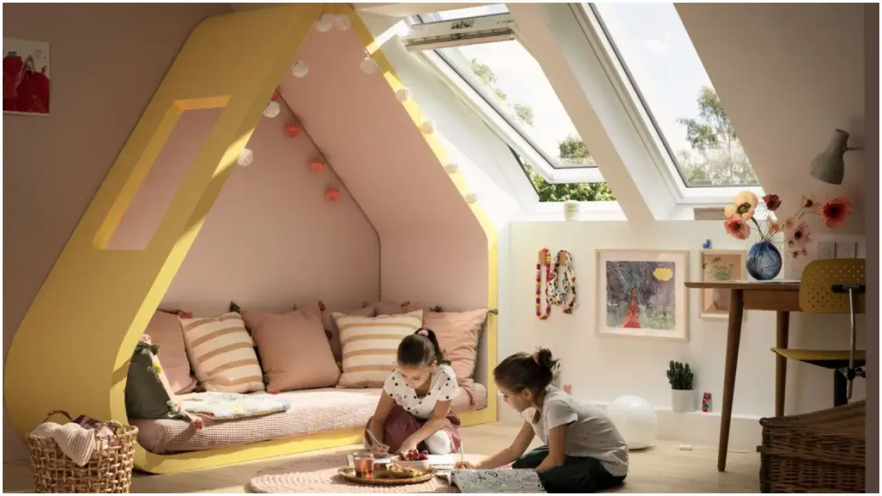 Dwie dziewczynki rysują w przytulnym pokoju na poddaszu. Jasne okna dachowe dodają uroku, a ich montaż to inwestycja w komfort.