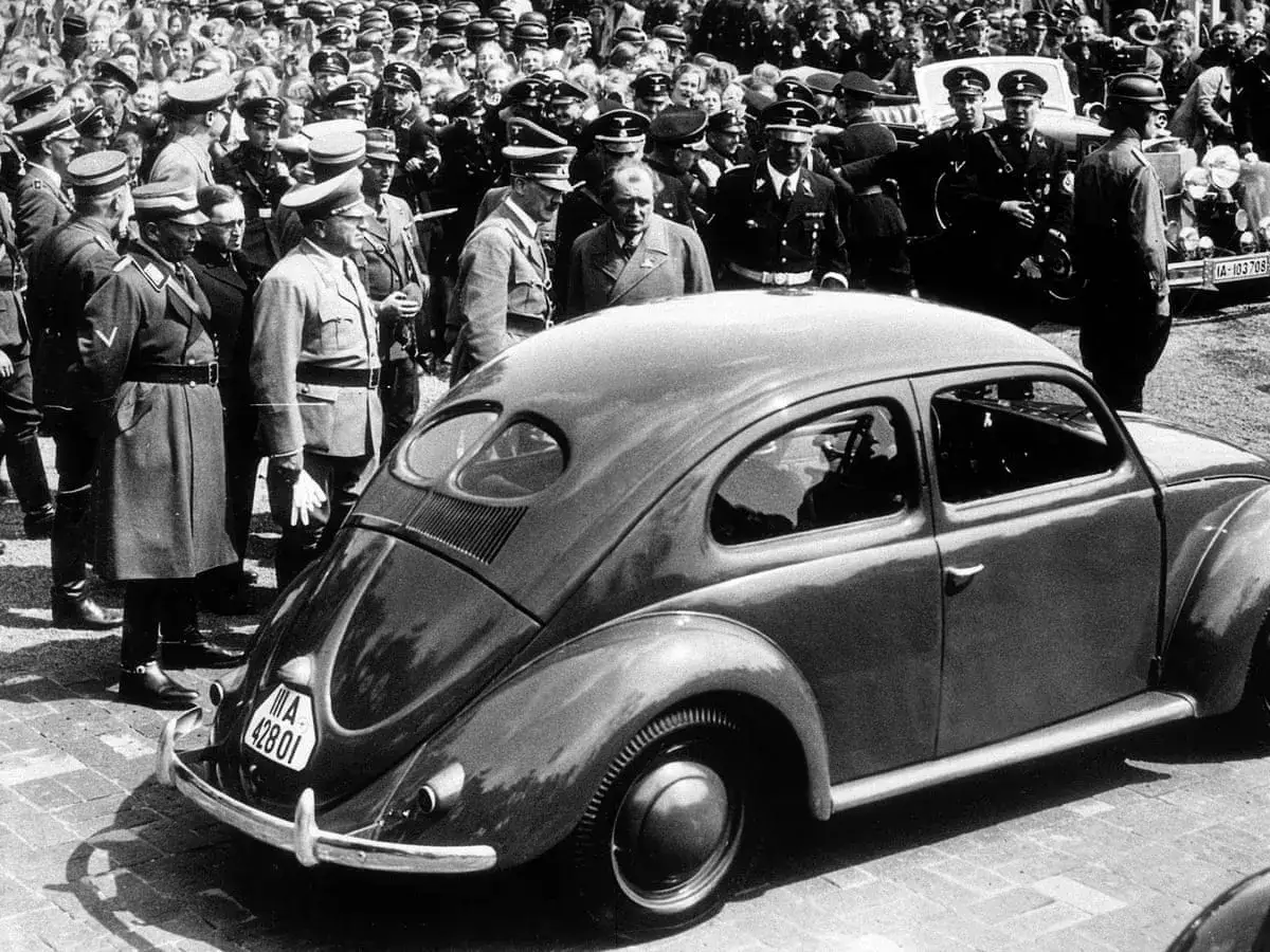 Volkswagen Garbus, znany z wielu nazw modeli, prezentowany w tłumie mężczyzn w mundurach.