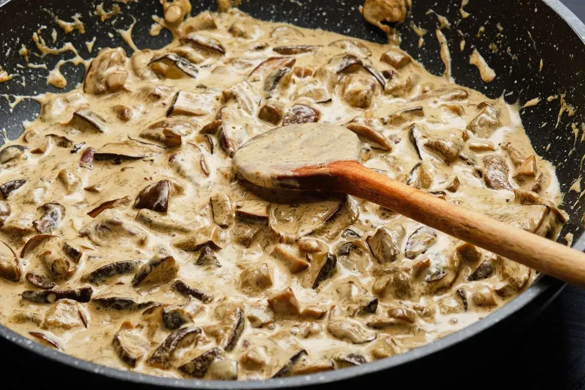 Kremowy sos pieczarkowy z mascarpone w patelni, mieszany drewnianą łyżką.