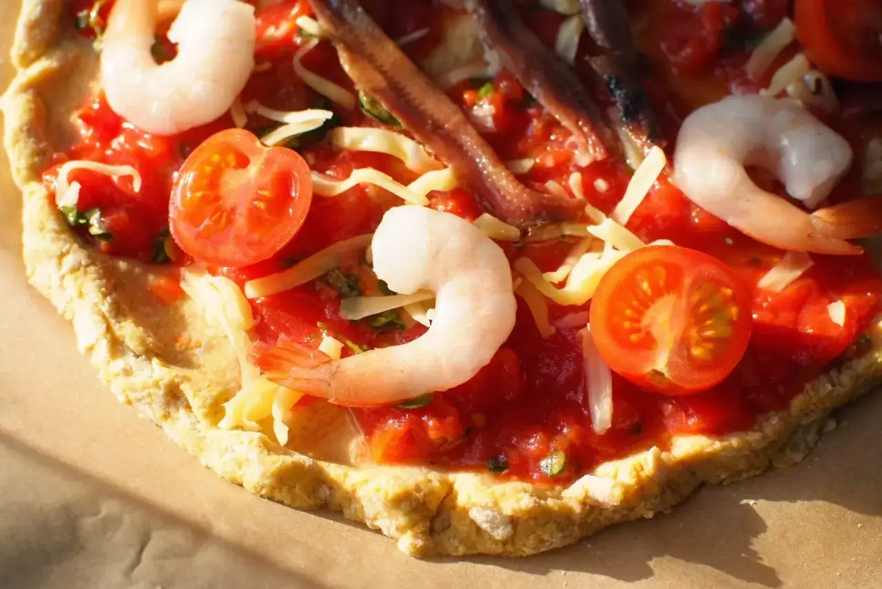 Pyszna pizza z krewetkami, pomidorkami i anchois, posypana serem.