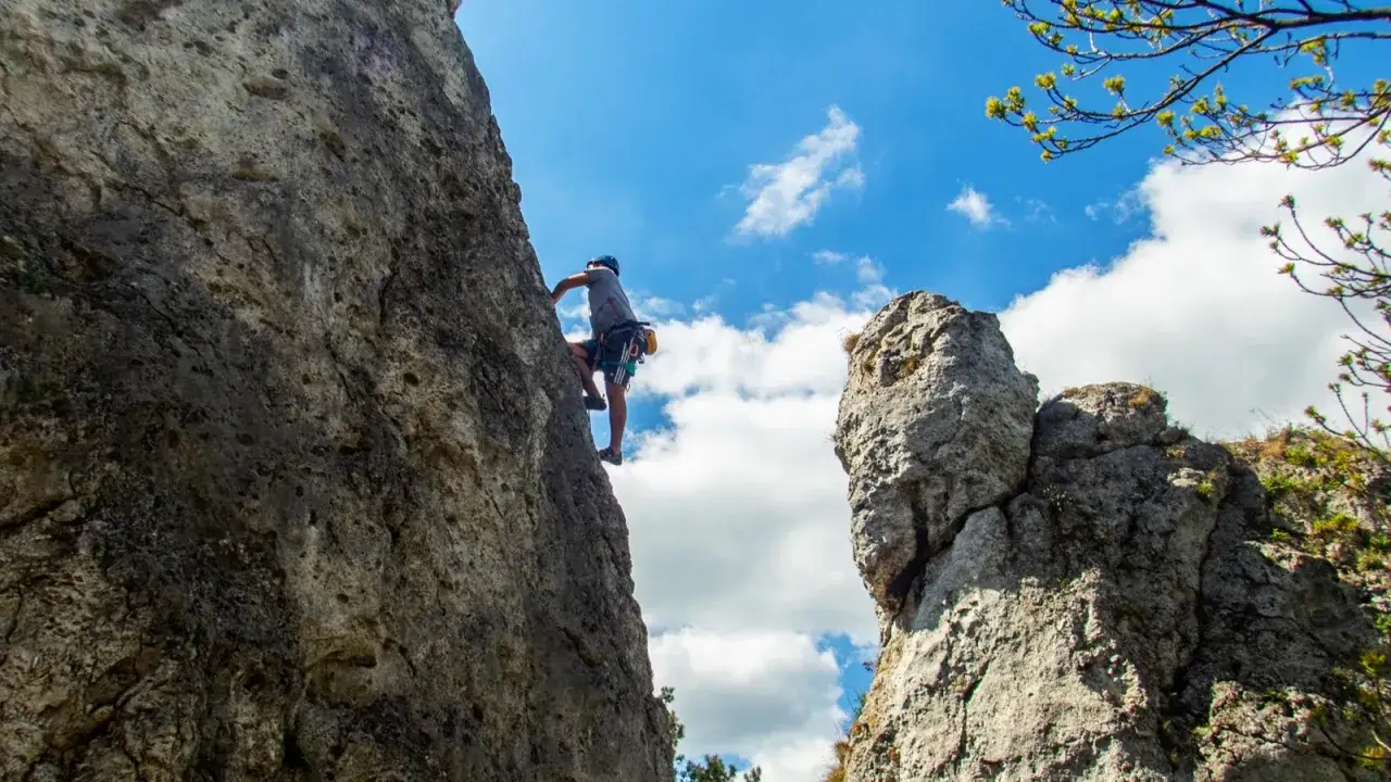 Wspinacz na skale podczas kursu taternickiego. Niebieskie niebo z chmurami.