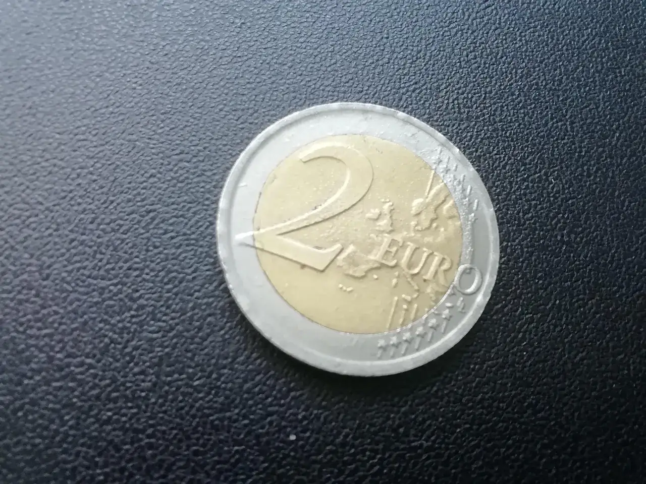 Moneta dwueuro, kt&oacute;ra jest walutą w Kosowie, leży na czarnej, teksturowanej powierzchni.