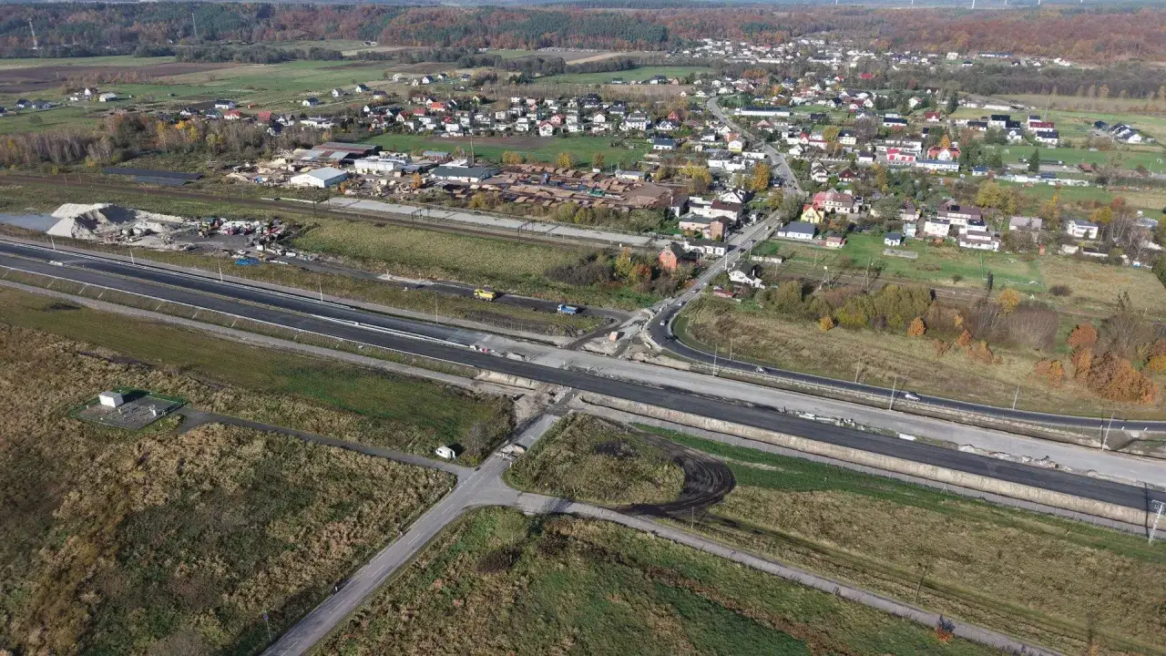 Widok z lotu ptaka na budowę drogi i osiedle domów. W oddali las i wiatraki. Tak wygląda gdzie jest Rumia w Polsce.