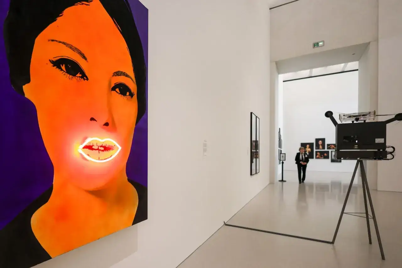 Wystawa w muzeum sztuki nowoczesnej: neonowe usta na portrecie i zabytkowa kamera filmowa.