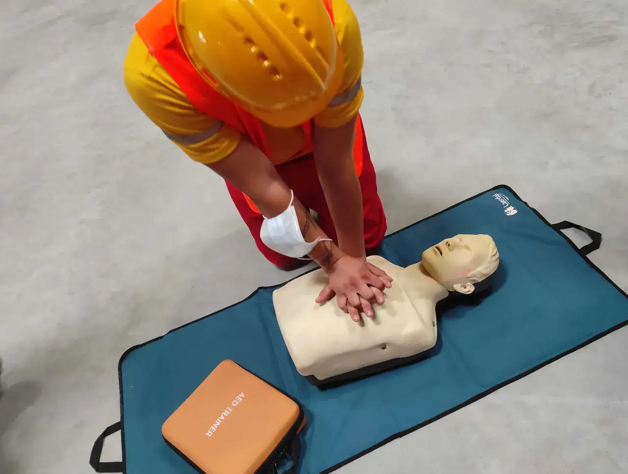 Osoba w kamizelce odblaskowej i kasku ćwiczy resuscytację na fantomie. To pokazuje, kto może prowadzić kurs pierwszej pomocy.