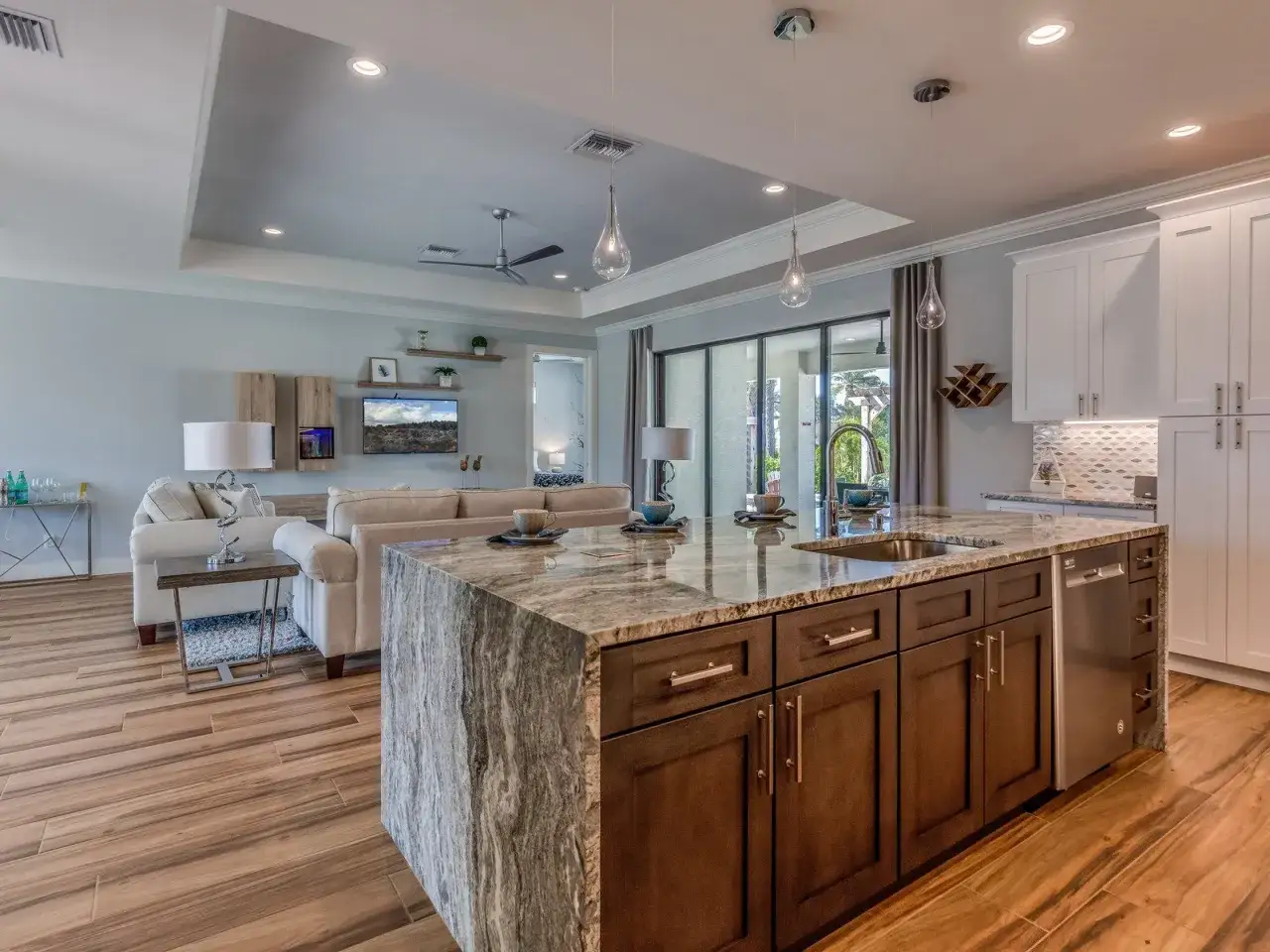 Nowoczesna kuchnia z wyspą i salonem. Ciepłe kolory drewna na podłodze i meblach tworzą przytulną atmosferę.