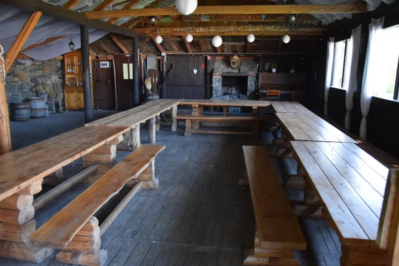 Wnętrze bac&oacute;wki agroturystycznej z drewnianymi stołami i ławami, idealne na spotkania.