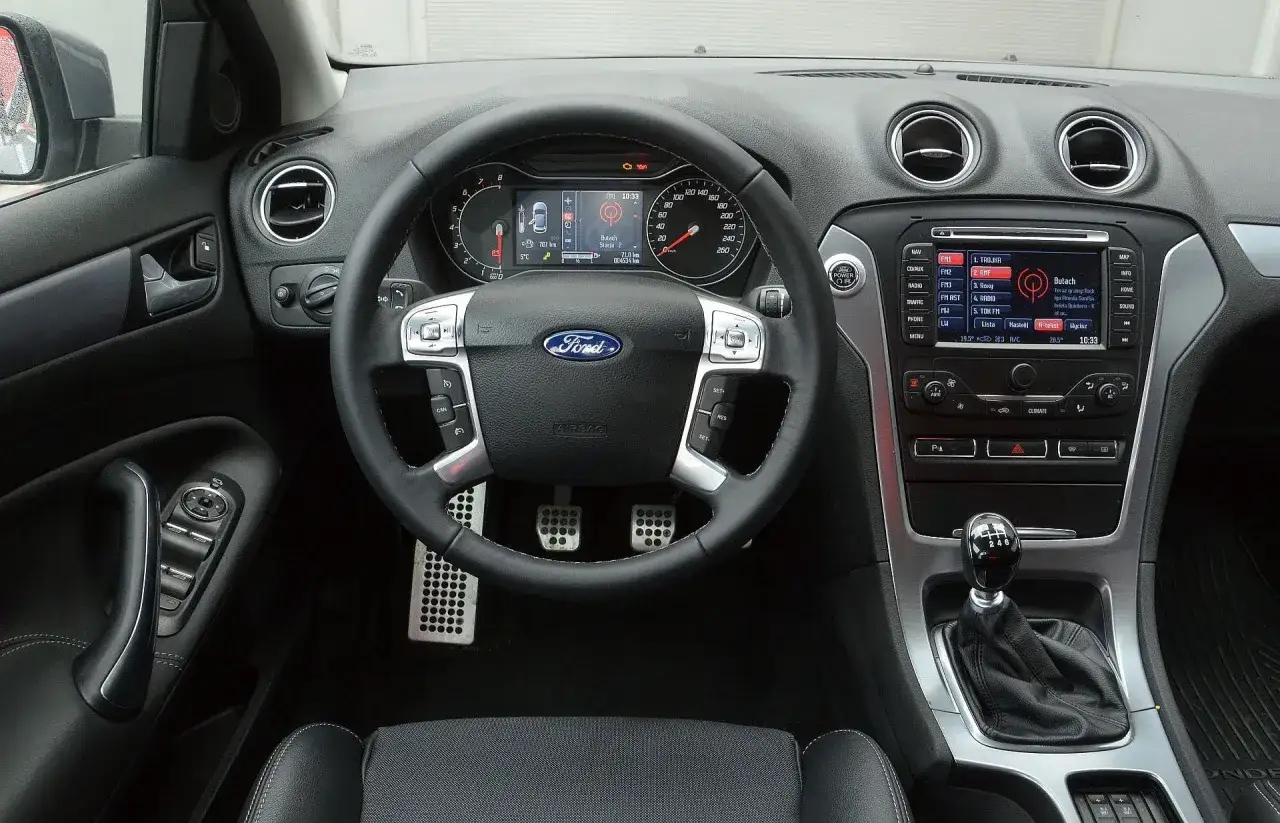 Wnętrze Ford Mondeo MK5: kierownica, deska rozdzielcza z ekranem multimediów i panelem klimatyzacji, dźwignia zmiany biegów.
