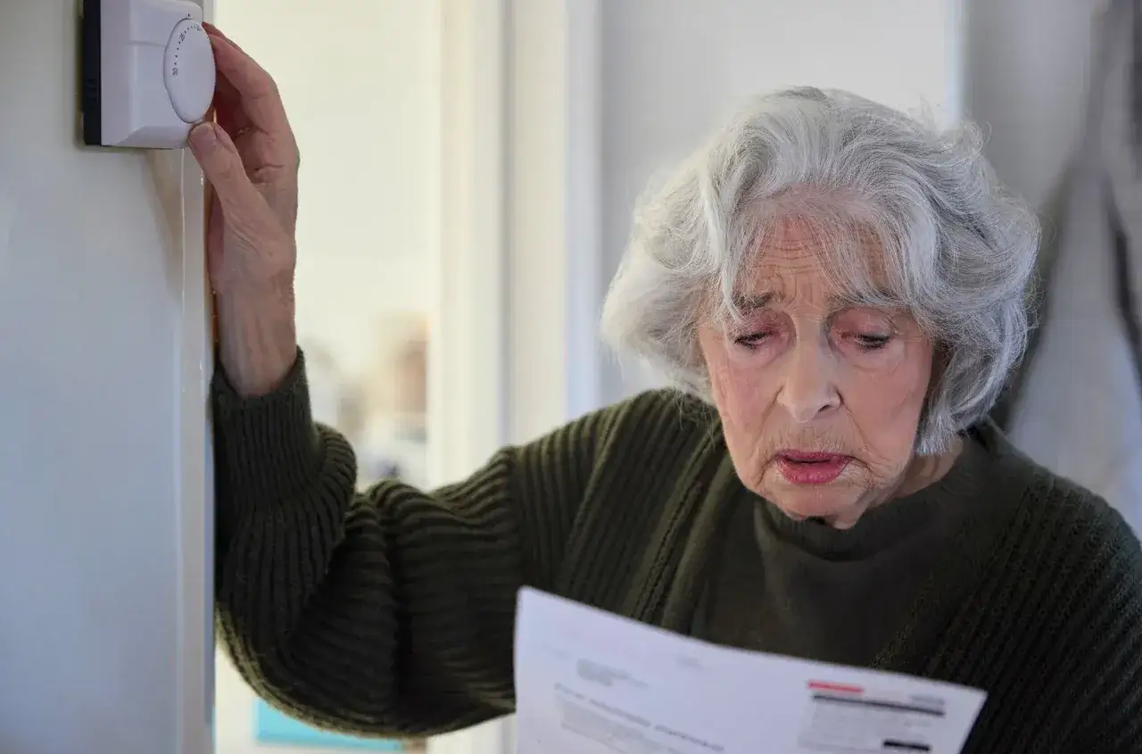 Zmartwiona emerytka sprawdza rachunki, regulując termostat. Czy złożyła wniosek o zniżki na prąd?