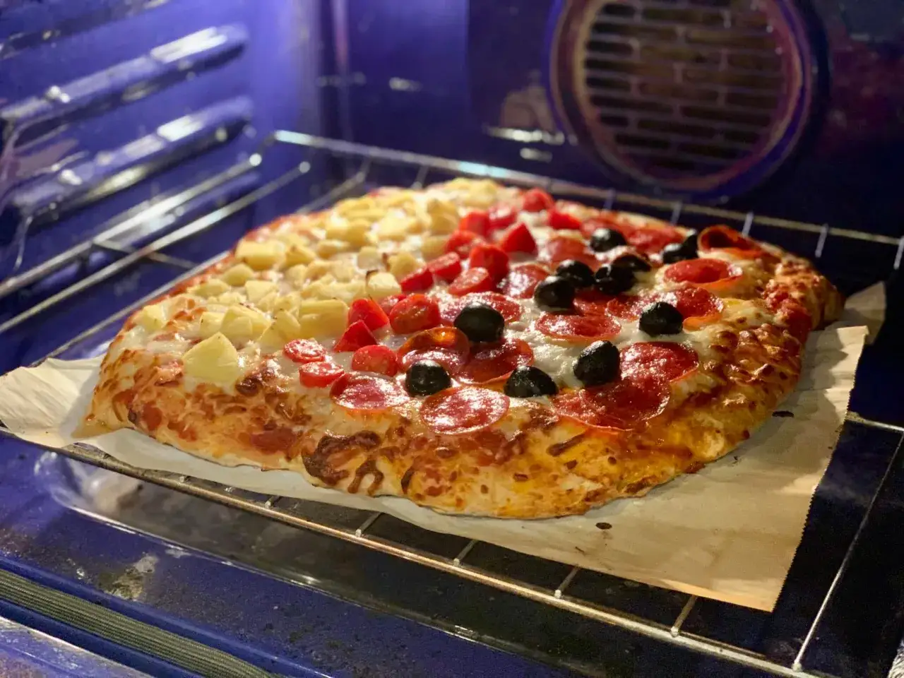 Pieczenie pizzy w 200 stopniach. Pizza z ananasem, pomidorkami i oliwkami na ruszcie piekarnika.