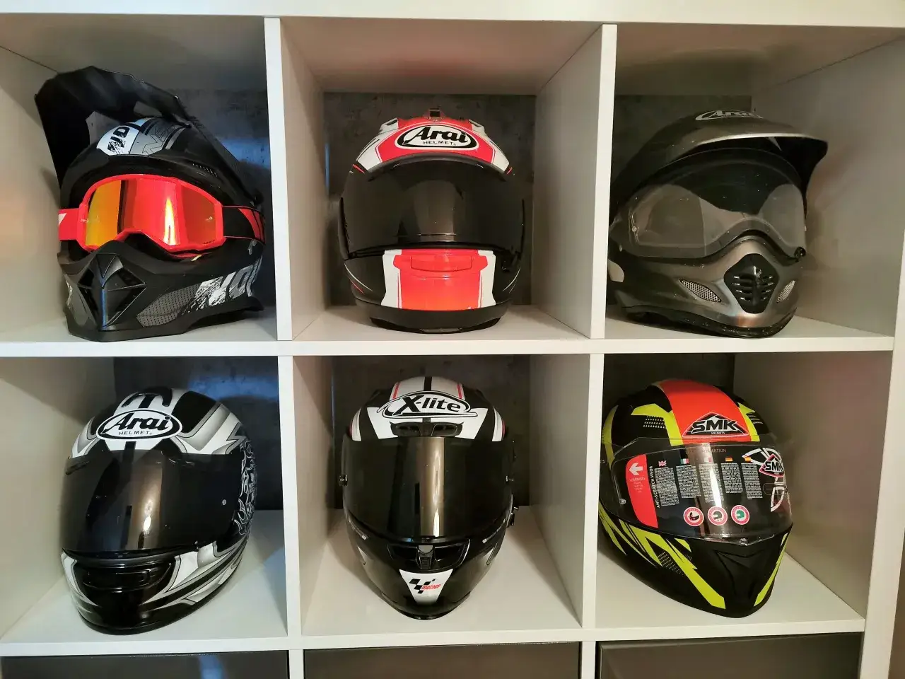 Kask szczękowy z goglami i kaski integralne, w tym Arai, X-lite i SMK, prezentują różnorodność ochrony motocyklisty.