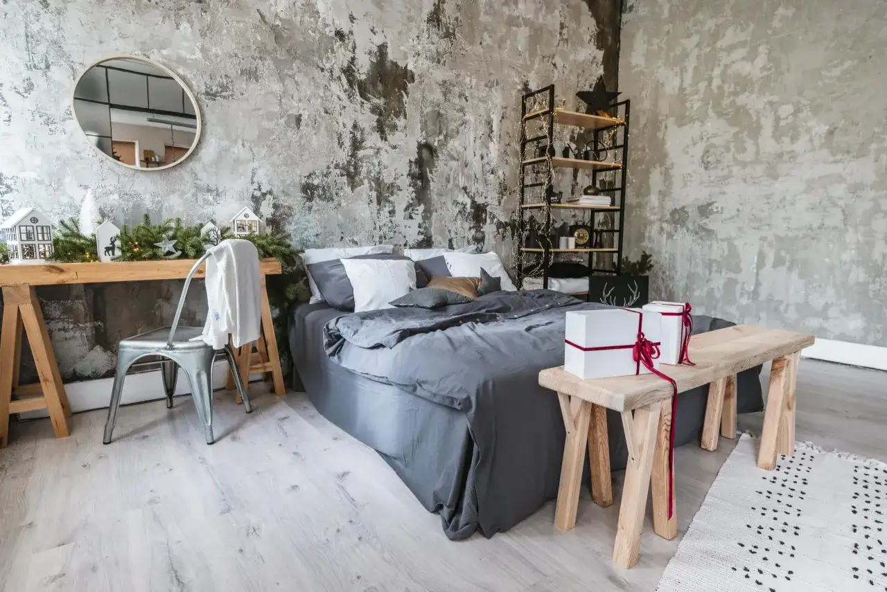 Męski pok&oacute;j inspiracje: surowe ściany, szare ł&oacute;żko, metalowe krzesło, drewniany stolik z prezentami i świąteczne dekoracje.