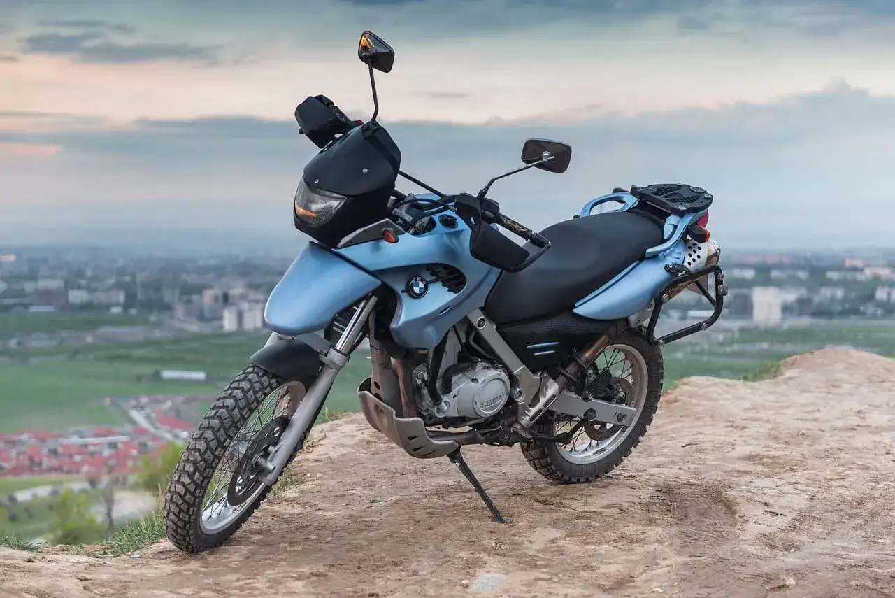 Niebieski motocykl BMW F650GS, idealny jako dobry motor szosowo turystyczny, stoi na wzgórzu z widokiem na miasto.