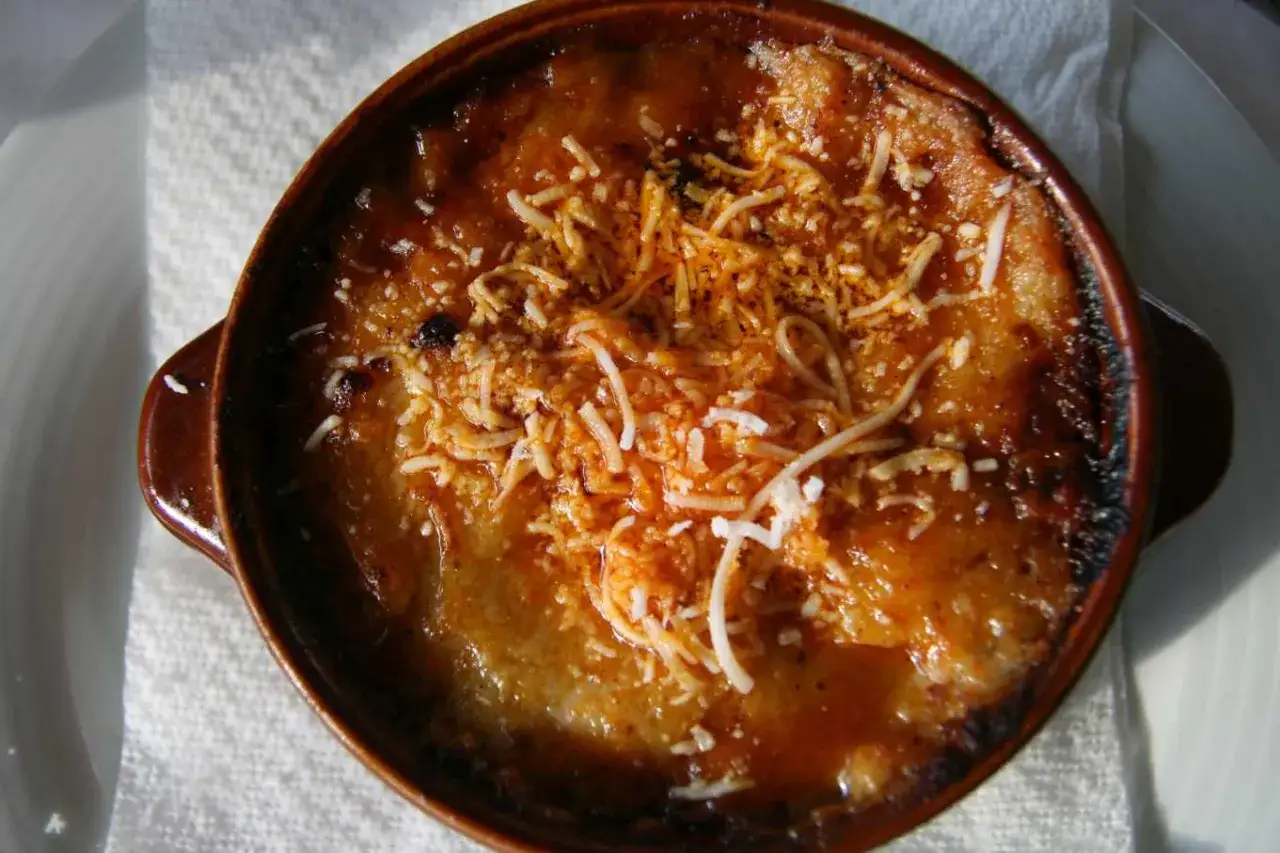 Pyszne, zapiekane **korfu jedzenie** w brązowej miseczce, posypane startym serem.