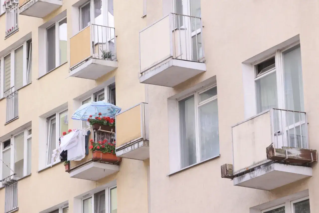 Na balkonie z parasolką i kwiatami suszy się pranie. Czy balkon to część wspólna? Okna i balkony bloku mieszkalnego.
