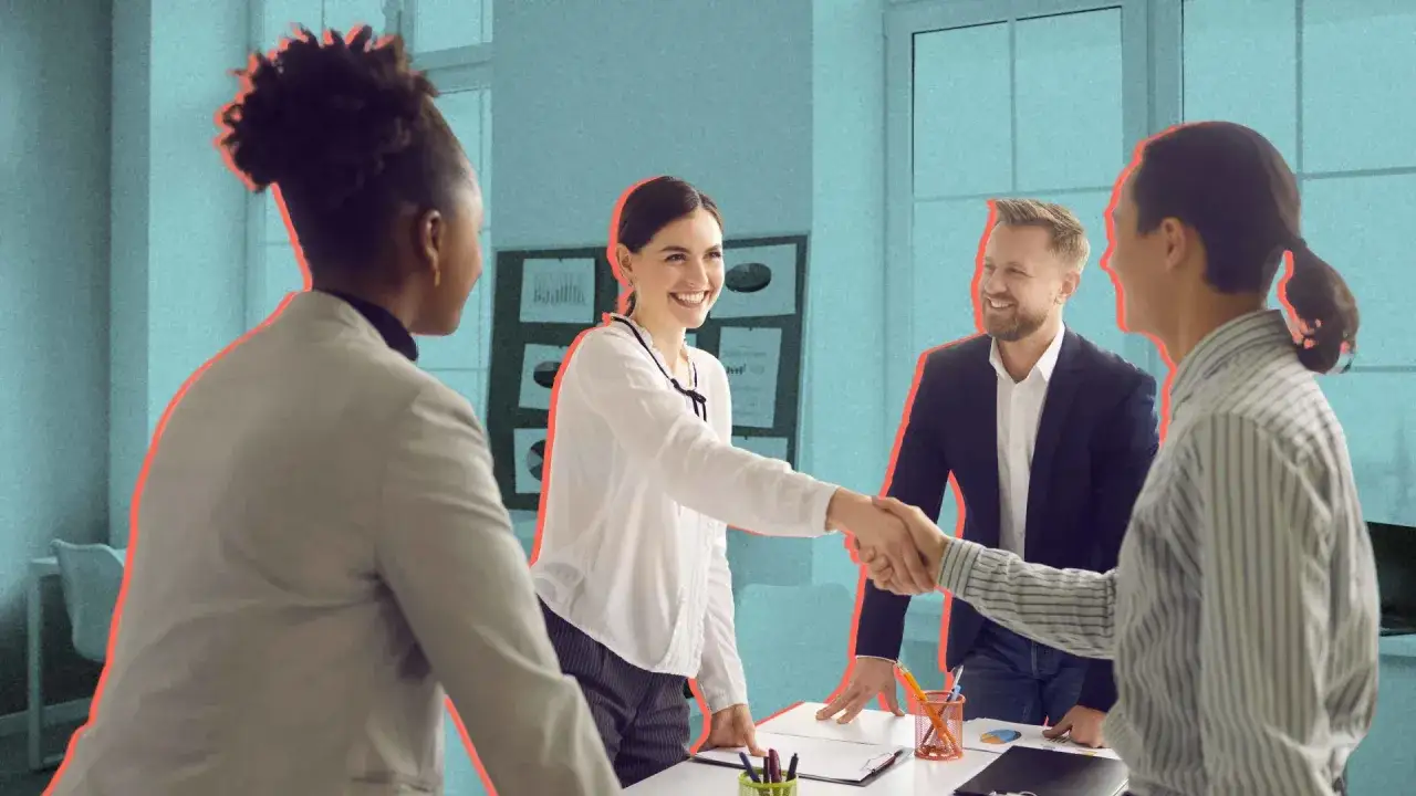 Uśmiechnięci ludzie w biurze, wymieniający uściski dłoni. To dobry moment na zadawanie pytań do poznania się i budowanie relacji.