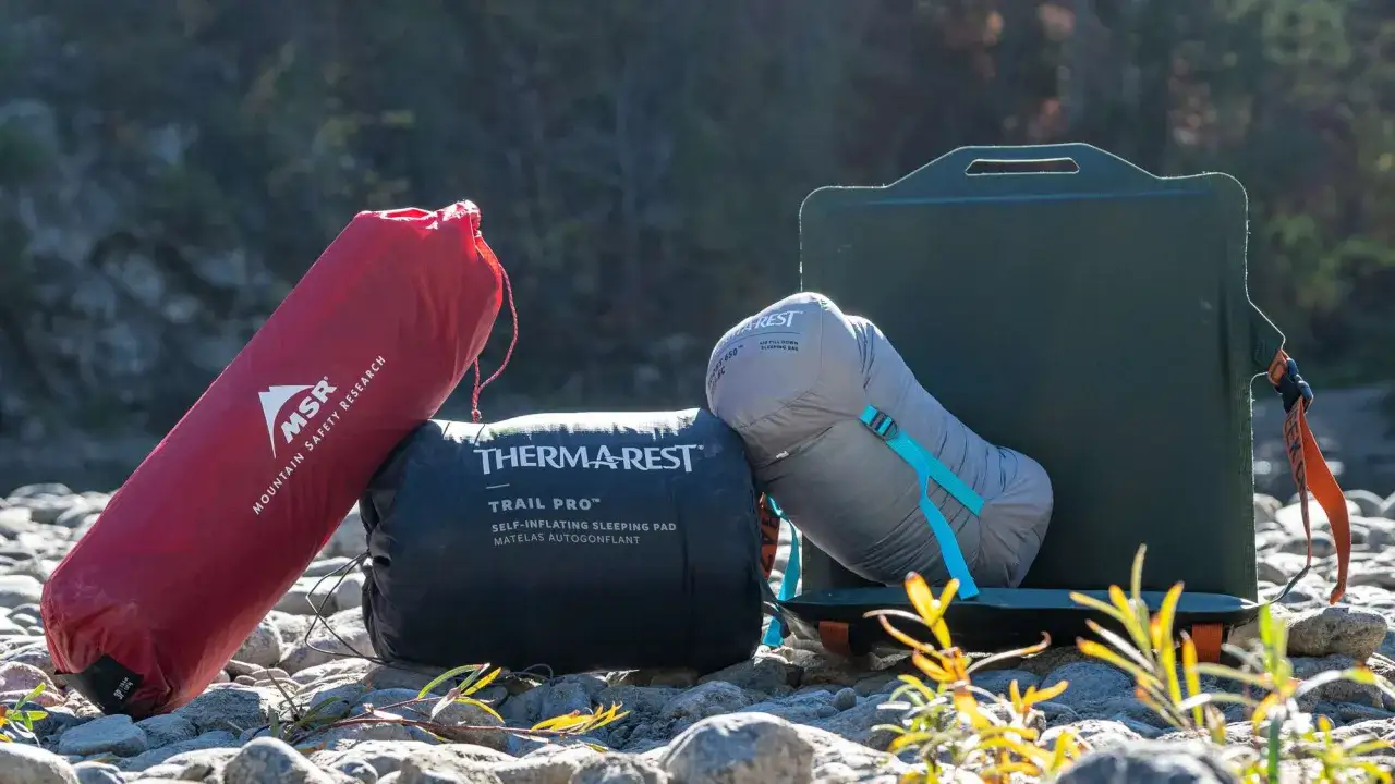 Niezbędne gadżety pod namiot: czerwony pokrowiec MSR, czarny materac Therm-a-Rest Trail Pro i szary śpiw&oacute;r Therm-a-Rest. Obok zielone siedzisko.