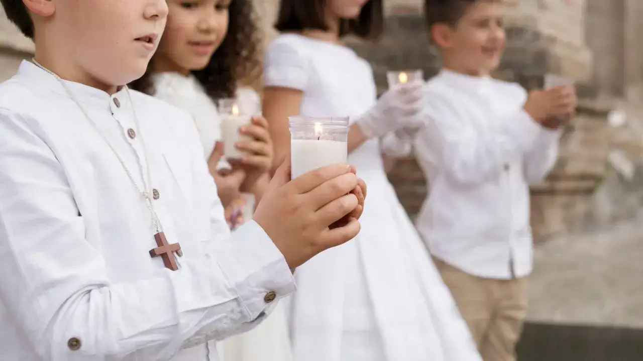 Dzieci w białych strojach z płonącymi świecami podczas komunii. Zastanawiasz się, ile kosztuje talerzyk na komunie?