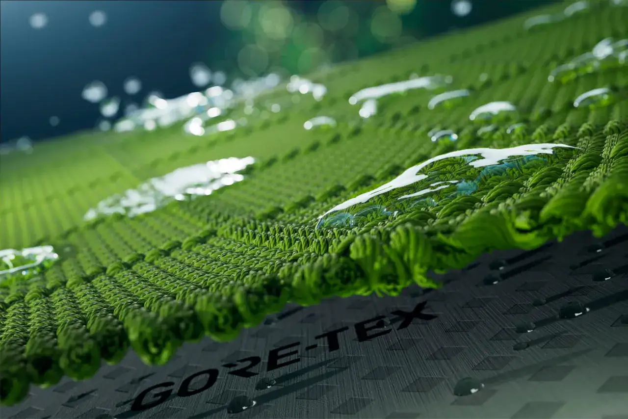 Krople wody odbijają się od zielonej, teksturowanej powierzchni. Widoczny napis GORE-TEX świadczy o wodoodporności.