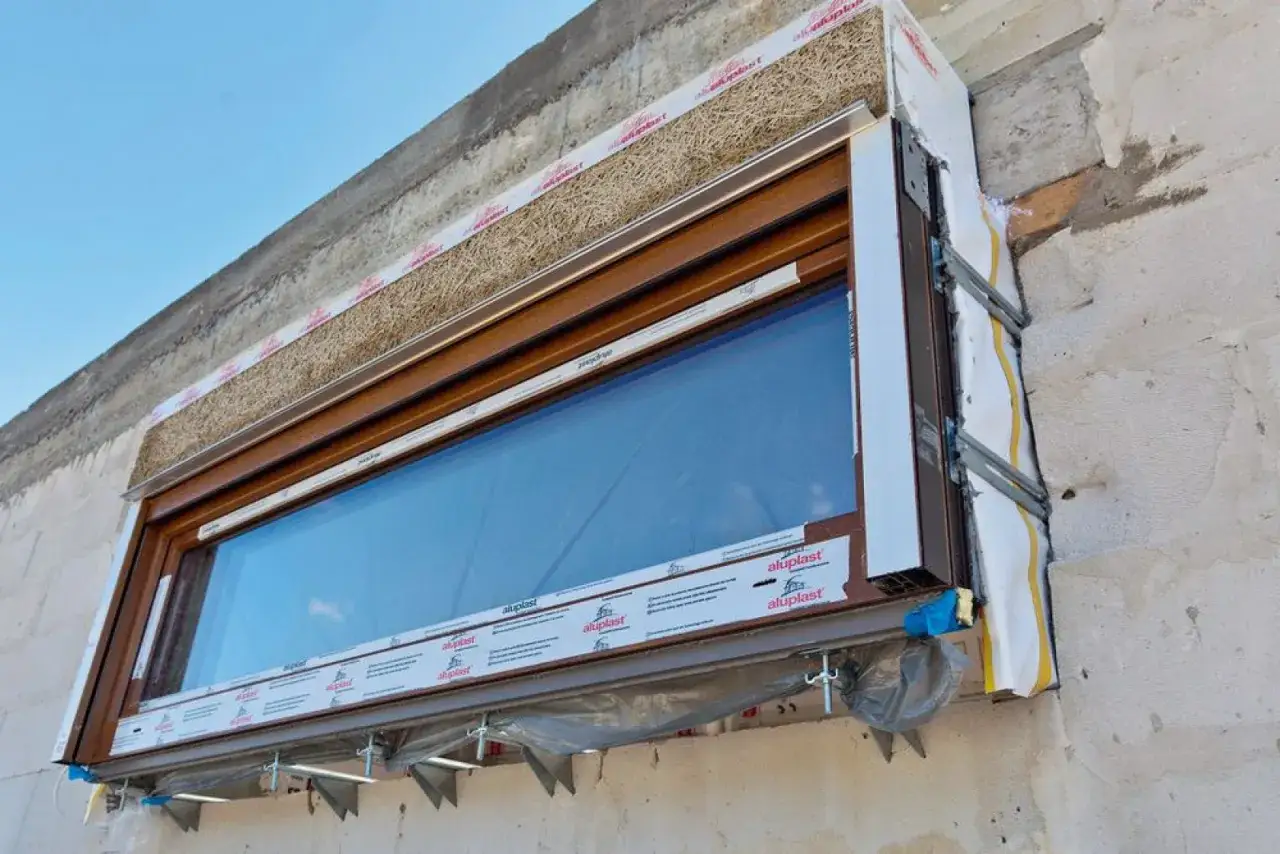 Montaż okna w ścianie z bloczków, z widoczną izolacją i elementami montażowymi. Czy odlicza się okna przy elewacji robocizna?