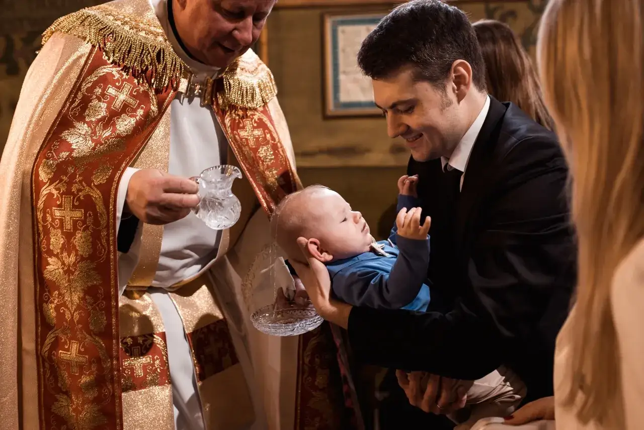 Ojciec trzyma dziecko do chrztu. Ksiądz w bogatej szacie z krzyżami trzyma dzbanuszek z wodą. Czy konieczna jest spowiedź przed chrztem?