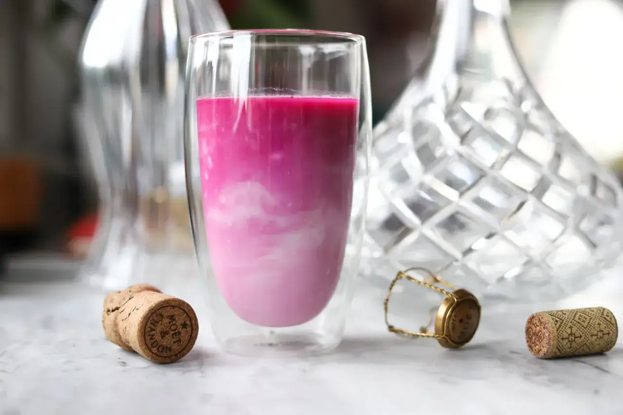 R&oacute;żowy nap&oacute;j w szklance, idealny kefir na kaca. Obok korki od szampana.