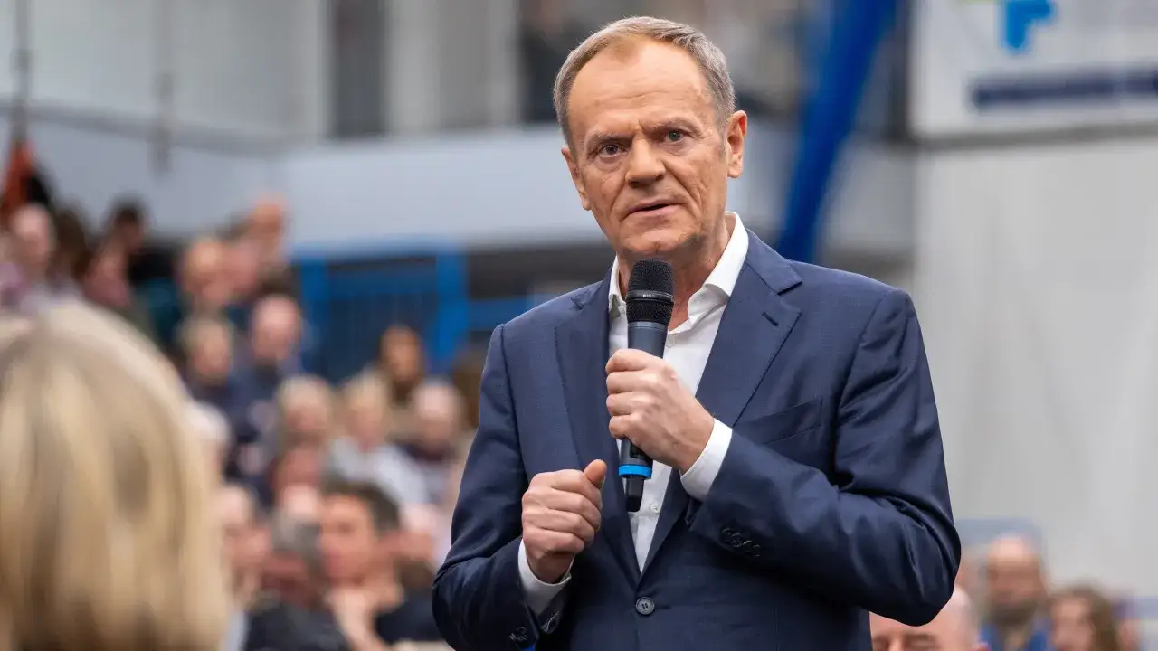 Donald Tusk przemawia do tłumu, trzymając mikrofon. W tle widać ludzi. Czy zastanawiasz się, ile Tusk ma emerytury na rękę?