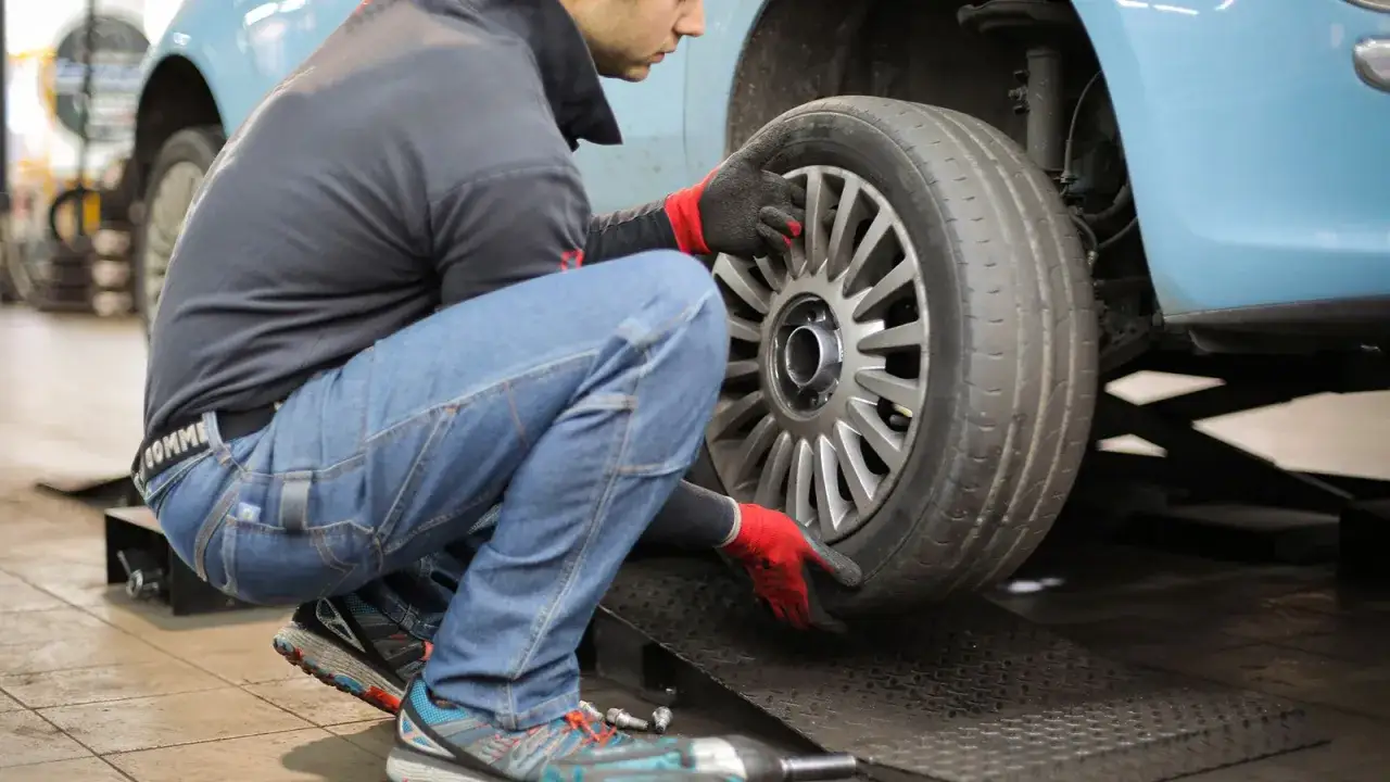 Mechanik w rękawiczkach zakłada koło do samochodu na podnośniku. To przykład, wulkanizacja co to jest – naprawa i wymiana opon.