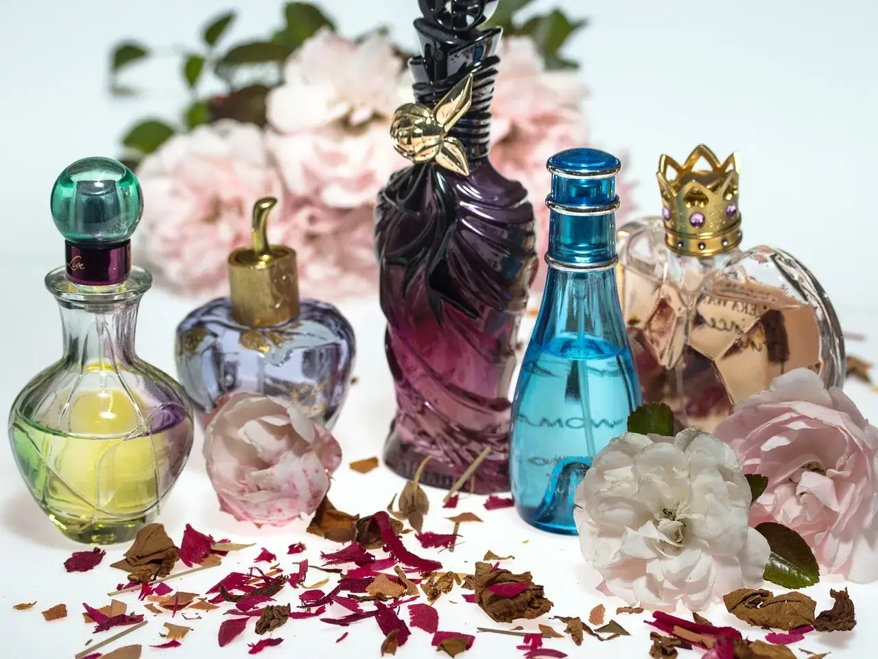 Inspiracja do stworzenia perfum z płatków róż: piękne flakoniki, róże i płatki na białym tle.