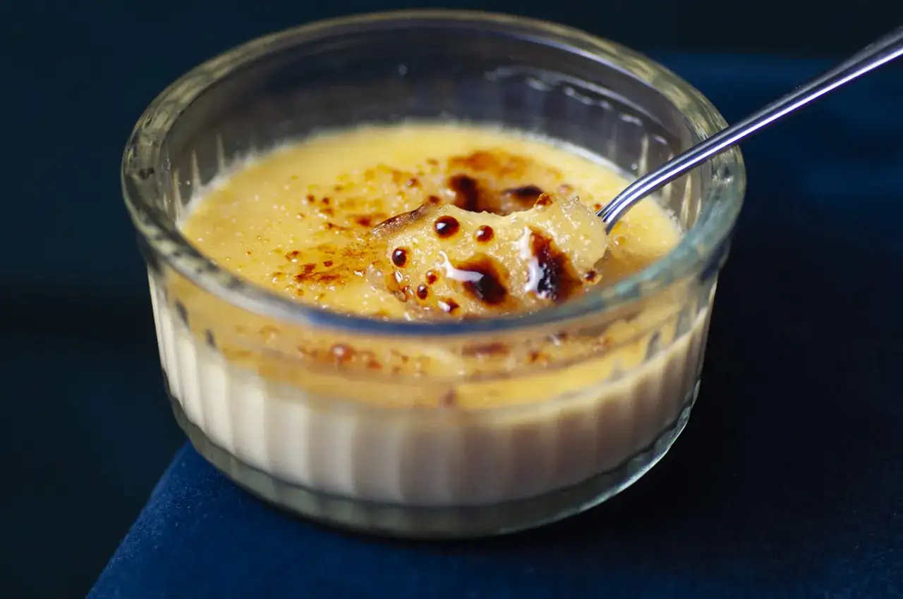 Idealny Crème Brûlée przepis: chrupiąca karmelizowana skórka i aksamitny krem. Łyżeczka zanurzona w deserze.