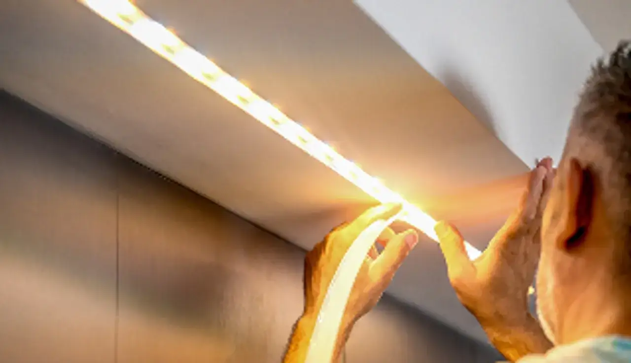 Instalacja taśmy LED 230V. Ręce montują świecącą taśmę wzdłuż sufitu.