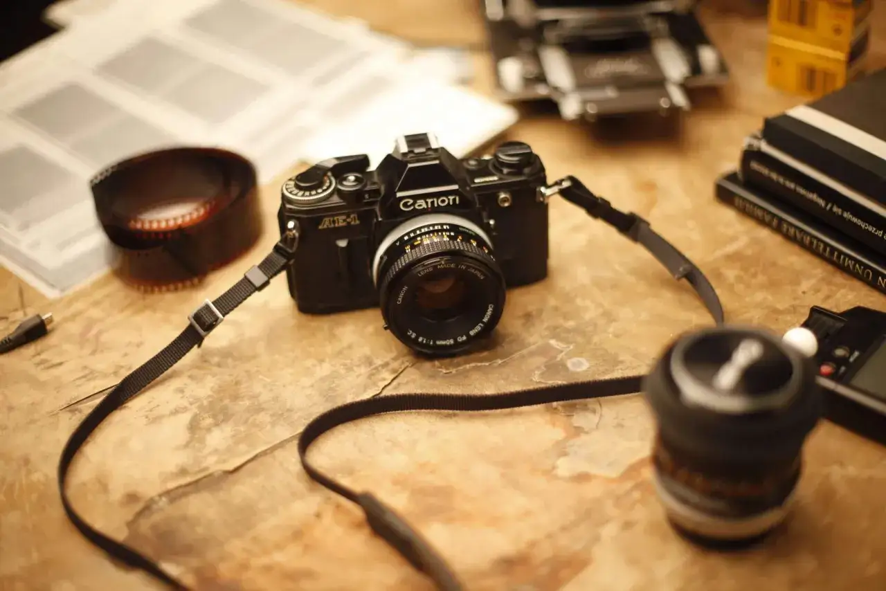 Klasyczny aparat Canon AE-1, rolka kliszy i książki o fotografii. Idealny zestaw do nauki w szkole fotografii.