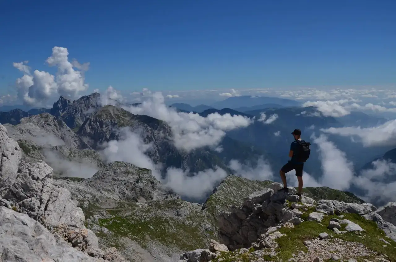 Turysta podziwia majestatyczne Alpy Kamnickie, otoczone chmurami i błękitem nieba.