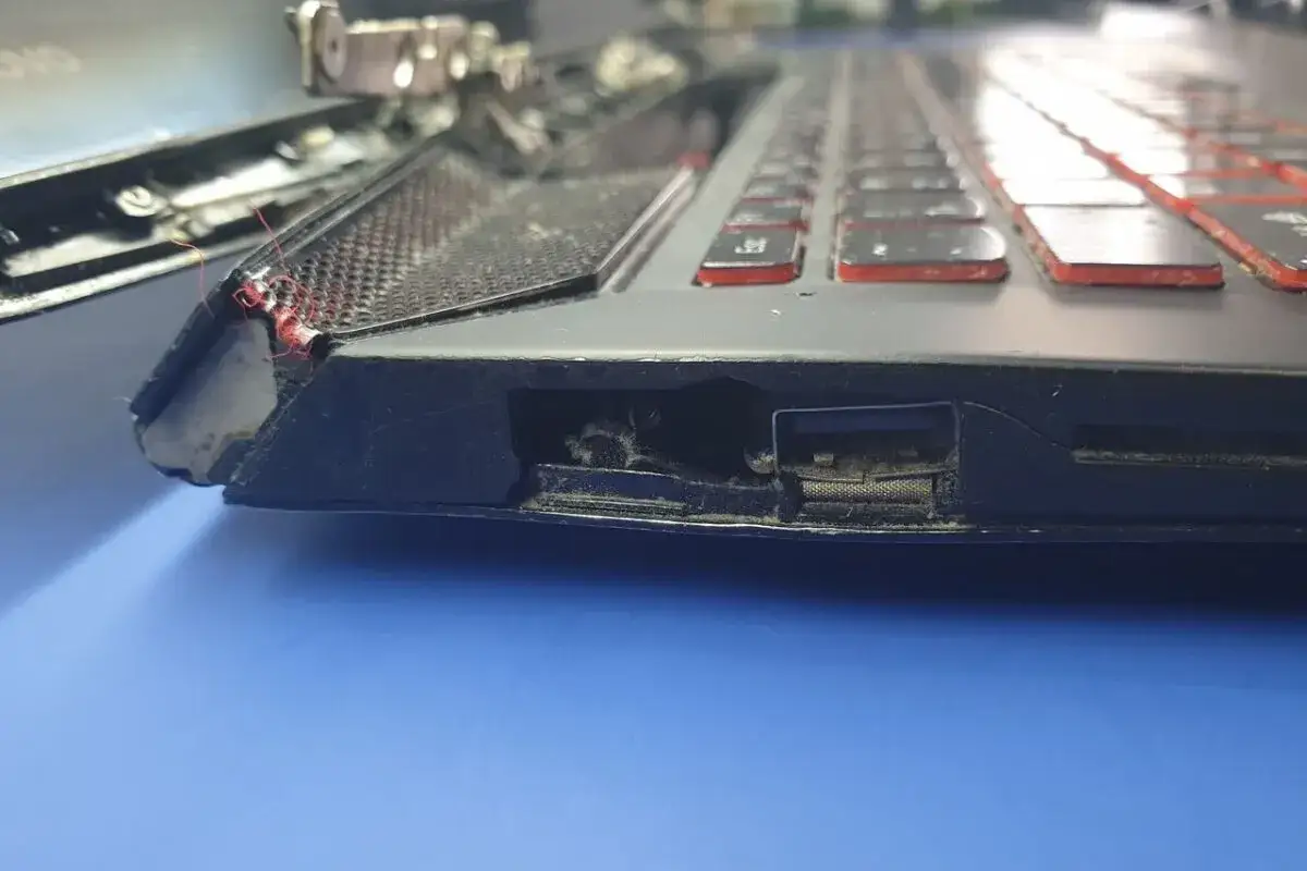 Uszkodzona bateria w laptopie objawy: wybrzuszenie obudowy, widoczne pęknięcia i luźne elementy. Widać też kurz i brud wewnątrz.