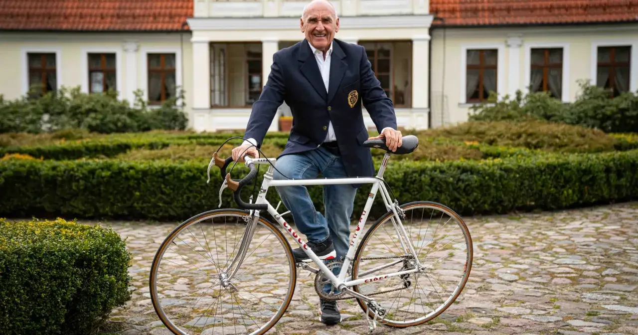 Uśmiechnięty Czesław Lang, który ma 78 lat, pozuje z rowerem przed pałacem.