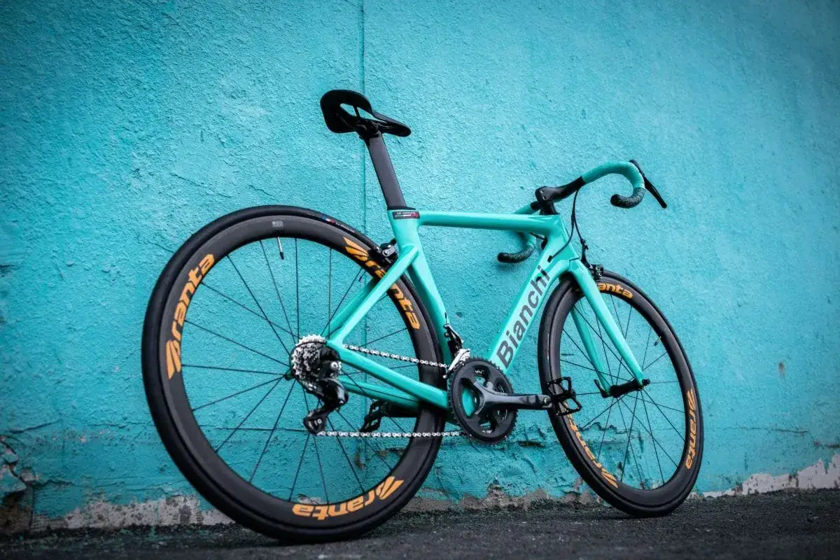 Turkusowy rower Bianchi z pomarańczowymi obręczami Aranta, oparty o ścianę. Choć Bianchi to znana marka, warto odkrywać też inne, mało znane marki rower&oacute;w.