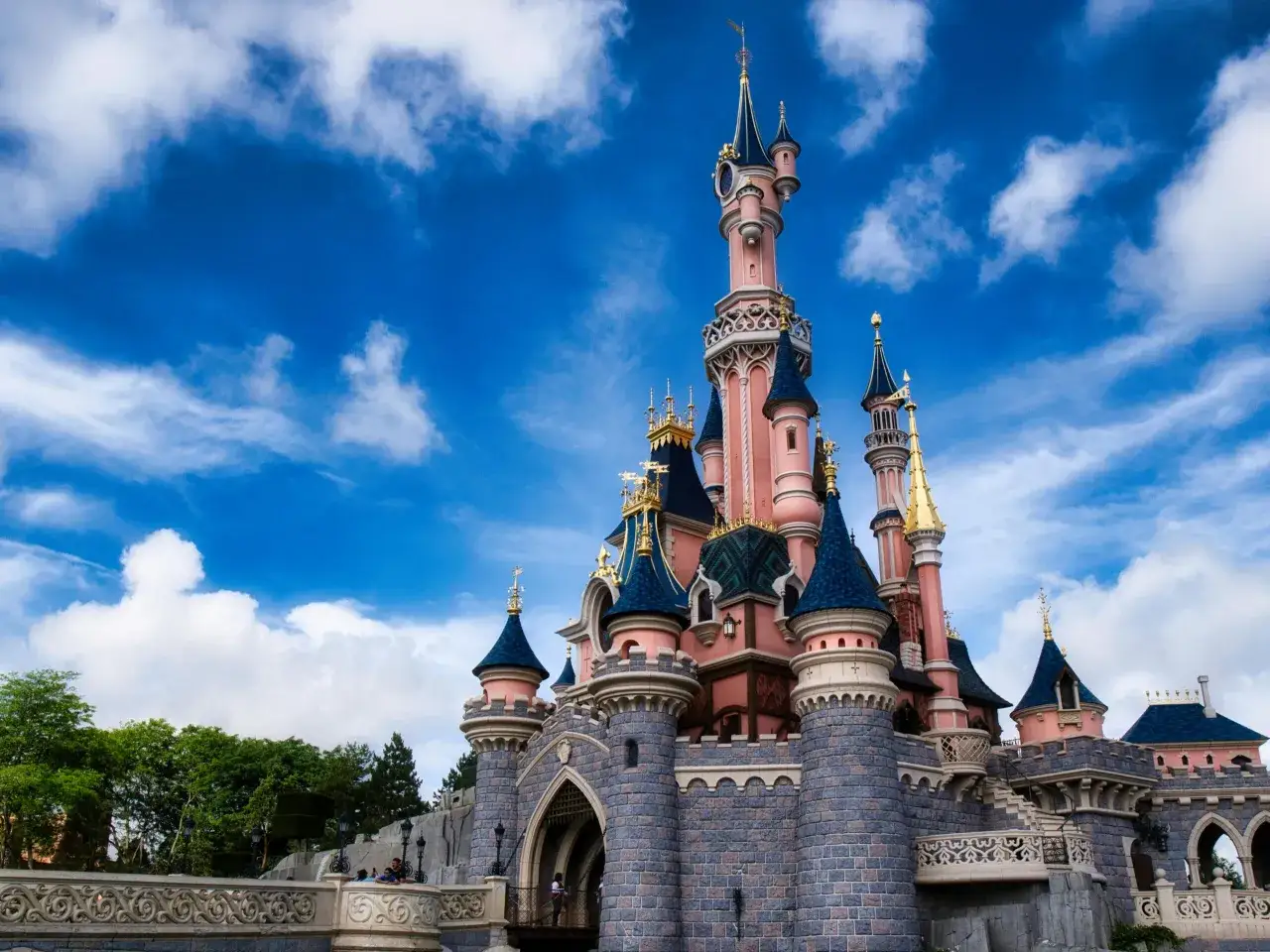 Bajkowy zamek, jedna z głównych atrakcji Disneylandu Paryż, wznosi się na tle błękitnego nieba z chmurami.