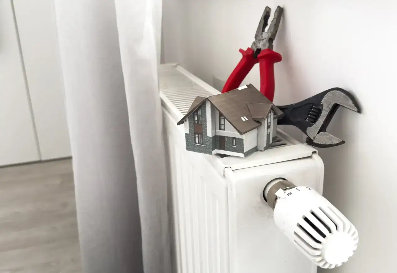 Model domu na grzejniku z kluczem i kombinerkami. Zastanawiasz się, ile bierze hydraulik za podłączenie pieca?