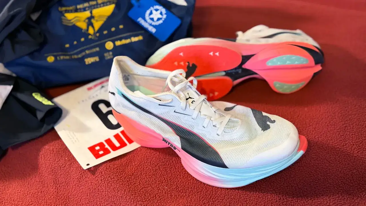 Białe buty do maratonu z różowo-niebieską podeszwą, obok numeru startowego i torby 