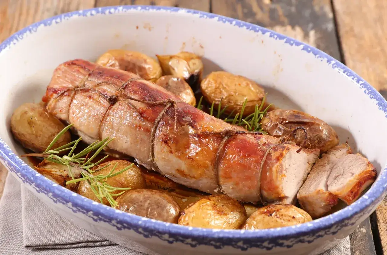 Pieczona poledwiczka wieprzowa z ziemniaczkami i rozmarynem w naczyniu żaroodpornym.