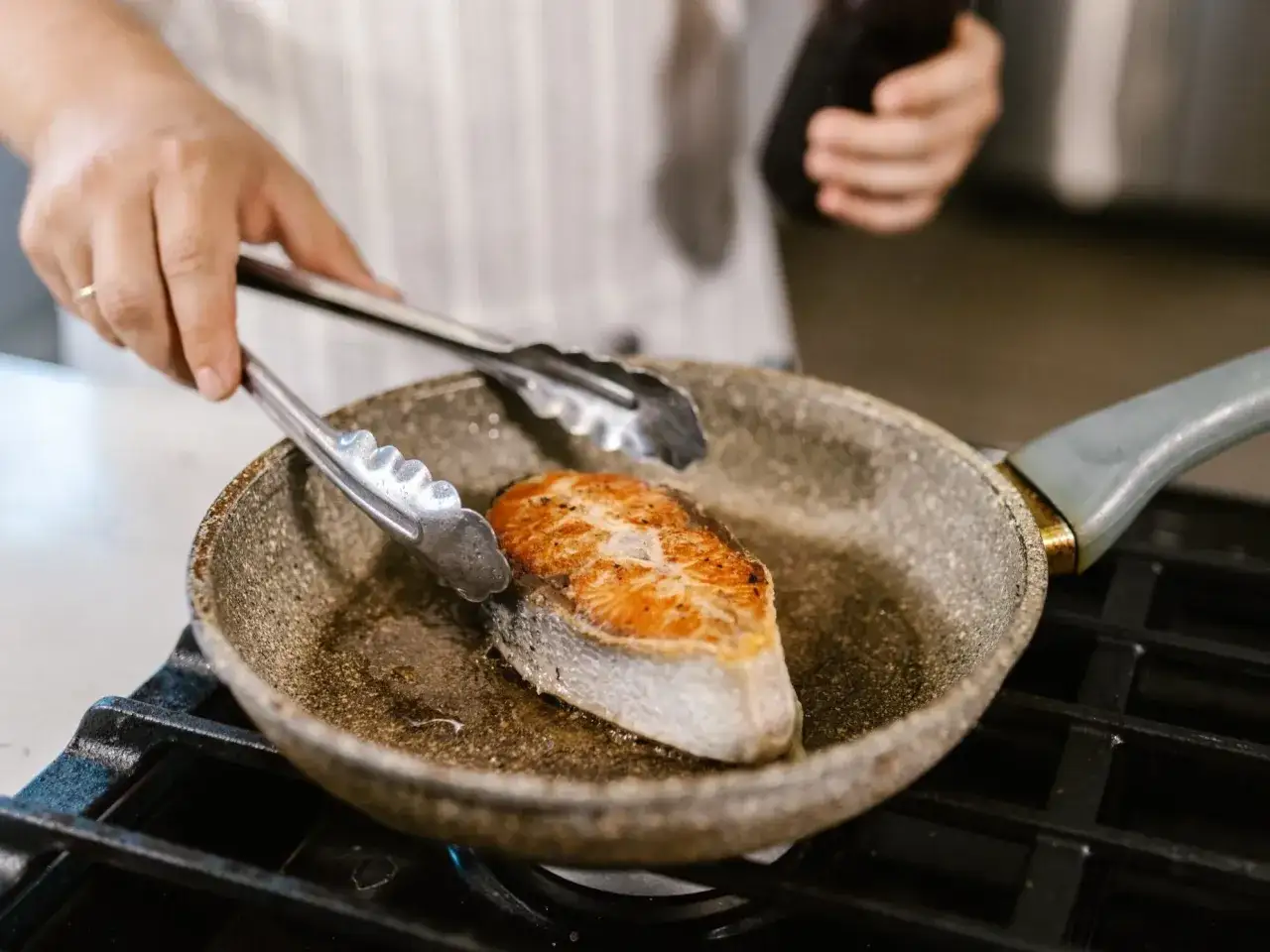 Kucharz sprawdzający widelcem usmażoną rybę