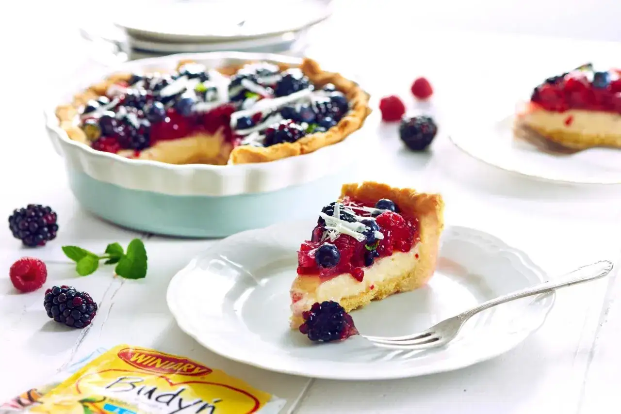 Prosta tarta z budyniem i owocami leśnymi, udekorowana wiórkami białej czekolady. Idealna na deser.