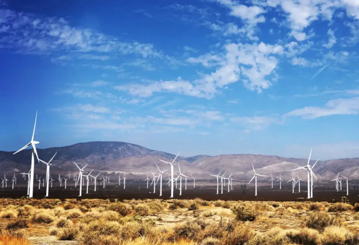 Wielka farma wiatrowa elektrownia na pustynnym krajobrazie pod błękitnym niebem z chmurami.