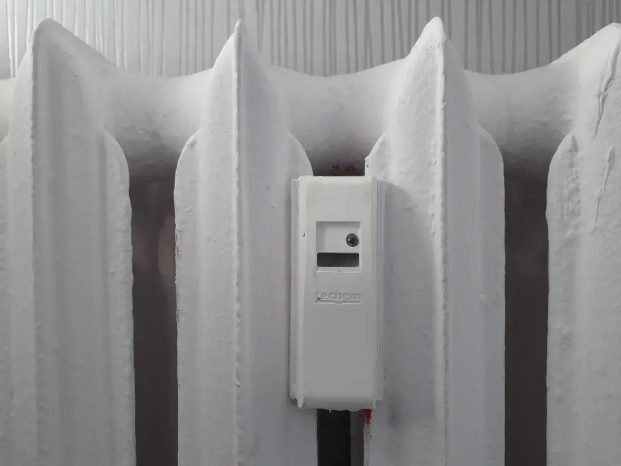 Biały grzejnik z zamontowanym podzielnikiem ciepła. To klucz do tego, jak obniżyć koszty ogrzewania w spółdzielni.