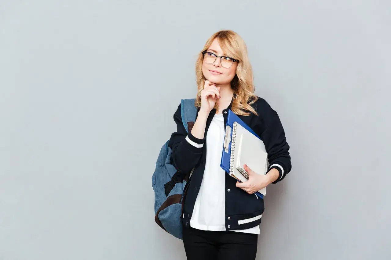 Młoda kobieta w okularach z plecakiem i zeszytami zastanawia się, co daje studium.