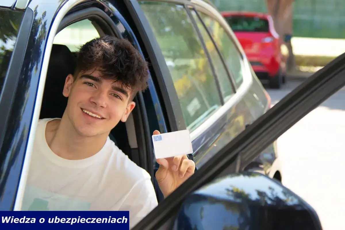 Uśmiechnięty młody mężczyzna, współwłaściciel samochodu poniżej 25 roku życia, trzyma dowód rejestracyjny.