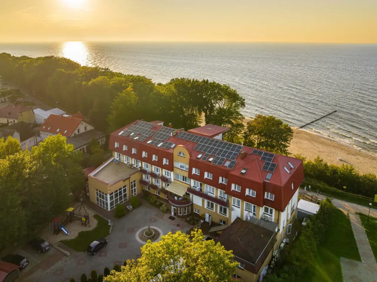 Ośrodek wypoczynkowy Jantar z panelami słonecznymi na dachu, położony blisko plaży i morza, otoczony zielenią.
